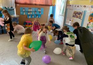 Eco-bal karnawałowy. Podczas konkursu, dzieci chwytają balony leżące na dywanie.